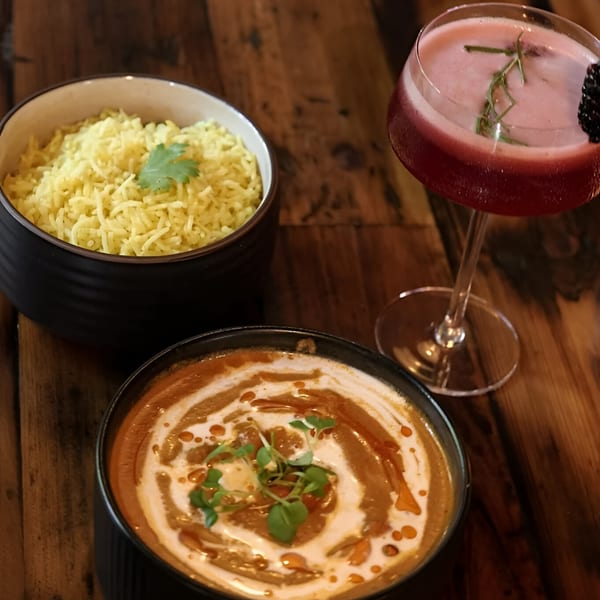 Indian butter chicken, yellow rice, and a red cocktail with a blackberry and rosemary garnish.