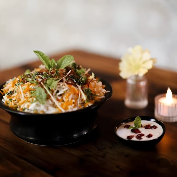 Aamrai Indian Kitchen's biryani in a black bowl with raita, a candle, and flower on a wooden table.