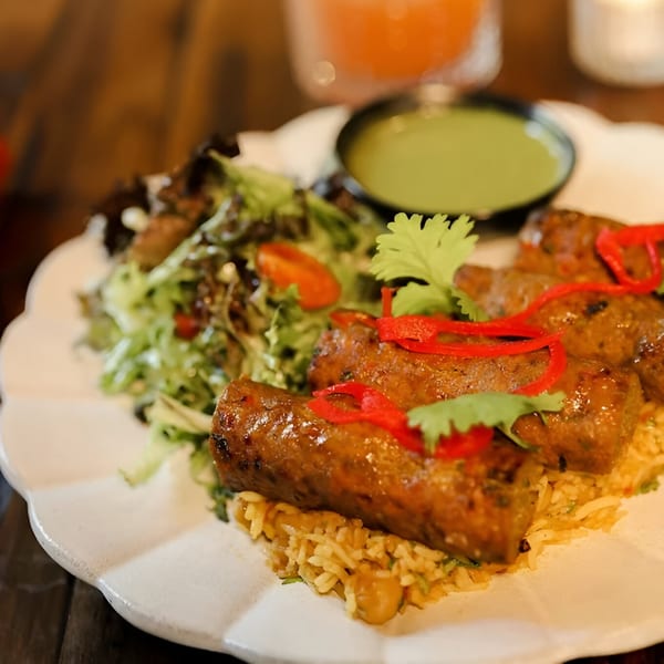 Indian seekh kebabs with rice, fresh salad, and green chutney on a white plate.