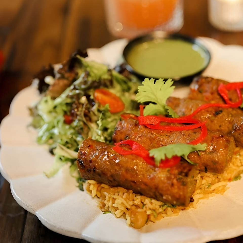 Indian seekh kebabs with rice, fresh salad, and green chutney on a white plate.