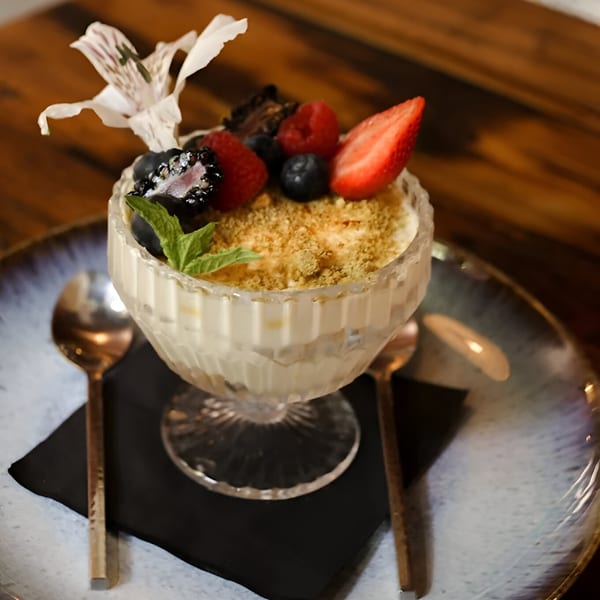 Aamrai Indian Kitchen And Bar's dessert, a creamy parfait topped with berries and a white flower.