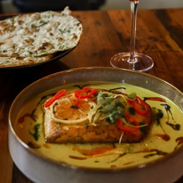 Indian salmon curry with naan bread and a glass of wine on a wooden table.