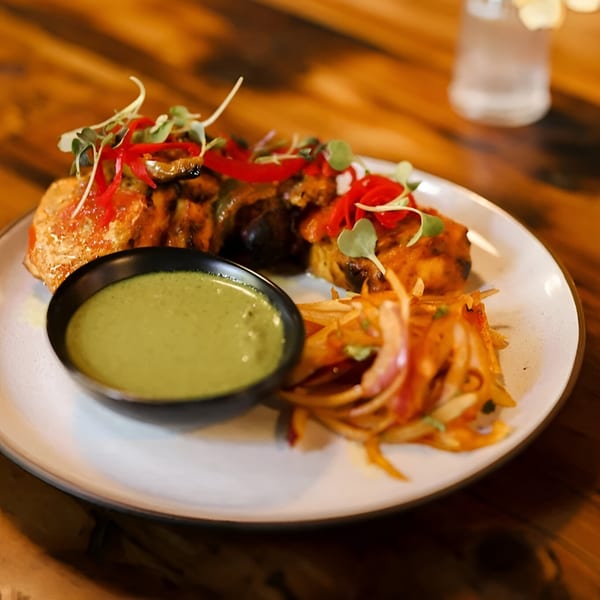 Indian chicken tikka with green chutney and pickled onions on a white plate.