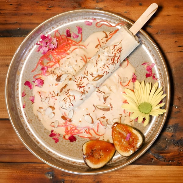 Indian kulfi popsicle with saffron, almonds, rose petals, and figs on a decorative plate.